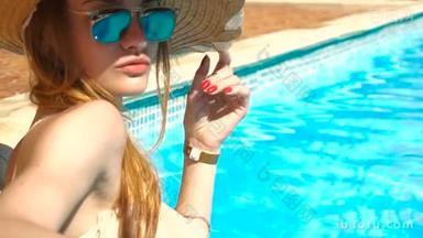 在草帽和太阳镜日光浴和游泳池里的女孩
